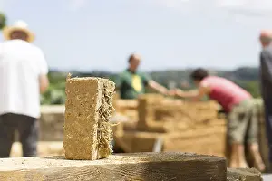 Labor Workforce Drucke: Mud brick in bio-construction and workers in the background out of focus
