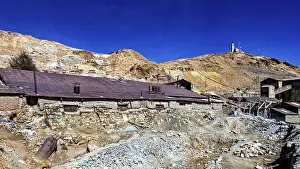 Potosi Drucke: Alte, verfallene Bergbaustrukturen vor einem trockenen Hügel unter einem klaren Himmel.