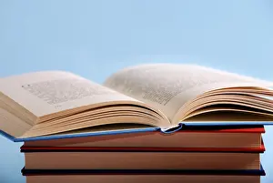 Plain Colored Background Photo Drucke: An open book on top of a stack of books against a light blue background