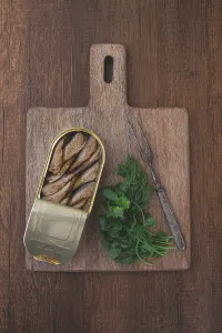 Drucke von Ein offener Spritzentopf, Vorspeise, auf einem Holzbrett, mit einer Gabel und Kräutern, Oberansicht Sprotte Drucke: Ein offenes Spritzengericht, Vorspeise.