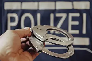 Crime Scene Drucke: A pair of handcuffs is held by one hand