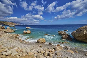 Pebble Beach Greece Drucke: Pebble beach with large rocks and gentle waves under a cloudy sky