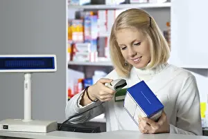 Female Pharmacist At Work Drucke: Pharmacist scanning medicine with barcode reader
