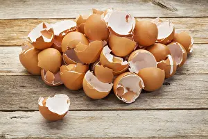 Broken Eggshells Drucke: A pile of broken empty brown chicken eggshells on a rustic wooden table