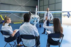 Aviation Education Drucke: Pilot instructor explaining aviation concepts to students in a hangar
