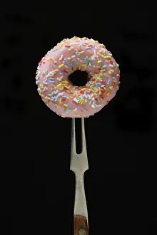 Unhealthy Sweet Treats Drucke: Pink donut on fork against black background