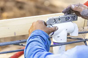 Construction Site Work Drucke: Plumber using level while installing PVC pipe at construction site