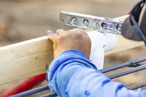 Construction Site Work Drucke: Plumber using level while installing PVC pipe at construction site