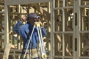 Young Construction Worker Drucke: Builder with dumpy level giving instructions