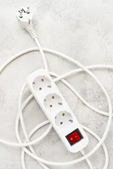Office Work Station Setup Drucke: Power strip with multiple sockets and a switch in a cluttered setup on a textured surface during daytime