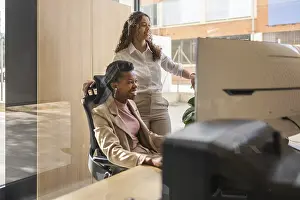 Office Teamwork Drucke: Two professionals are engaged at a computer in a bright office