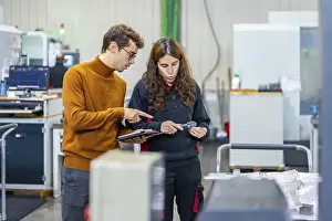 Young Professionals At Work Drucke: Quality control of two engineers standing and talking while using tablet in a cnc factory