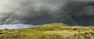 Prismatic Colors In Nature Drucke: Rainbow with dramatic rain clouds over dune landscape