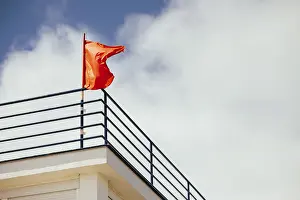 City View From Above Drucke: A red flag flutters on a rooftop railing against a backdrop of a cloudy sky