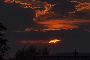 Central Europe Evening Mood Drucke: Red sun behind clouds in the evening sky