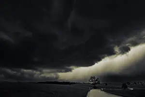 Straße und Wiesen mit Gewitterhimmel im Hintergrund.