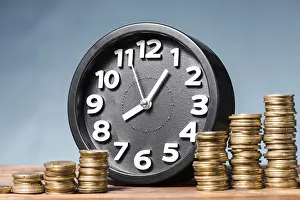 High Resolution Images Drucke: Round alarm clock with stack increasing coins against blue background