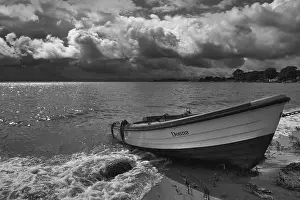 Deserted Sandy Beach Scene Drucke: Rowing boat on sandy beach in front of dramatic storm clouds