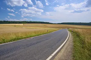 Agricultural Landscapes Drucke: Rural road through rolling fields under a blue sky with white clouds