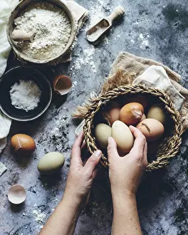 Ecological Food Photography Drucke: Rustic kitchen scene with hands holding a basket of assorted brown eggs
