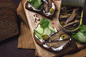 Drucke von Sandwiches, Schwarzbrot mit Sardellen, Sahne-Käse, Gurken, auf einem Schneidebrett, Oberansicht, Nahsicht, ohne Menschen Sprotte Drucke: Sandwiches, Schwarzbrot mit Sardellen.