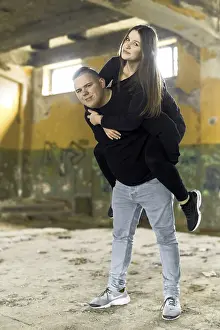 Straßenkunst Graffiti Drucke: Eine sanguine Frau spieltfreudig reitet auf einem optimistischen Manns Rücken in einem verlassenen Gebäude mit Graffiti