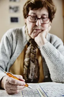 Leisure Activities For Adults Drucke: Senior sits at the table at home and solves puzzles