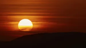 Greek Mediterranean Coastline Drucke: The setting sun breaks through dramatic layers of cloud and illuminates the silhouette of a hill
