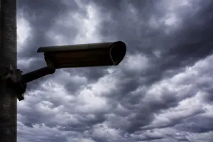 Cloudy Sky Photography Drucke: Silhouette of a surveillance camera against a dramatic
