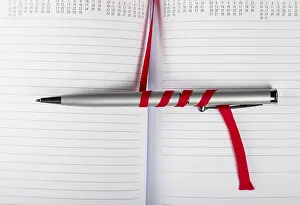 Office Supply Desk Utensils Drucke: Silver pen on opened notebook with red string