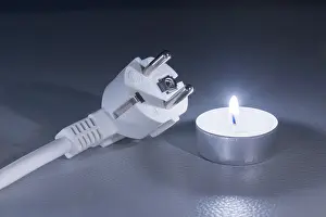 Dark Background Concept Drucke: A single candle next to an electrical plug on a dark background
