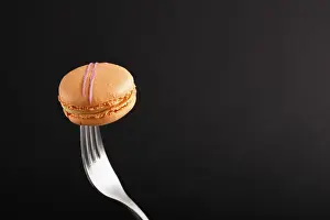 Pastel Colored Desserts Drucke: Single orange macaron or macaroon cake on a fork on black background