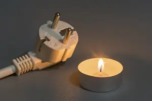 Power Failure Concept Drucke: Small burning candle next to electrical plug on dark background