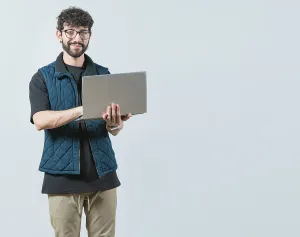 Young Man With Laptop Drucke: Smiling Bearded guy using laptop and looking at camera isolated