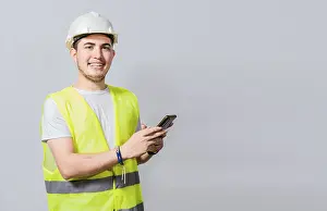 Young Engineer Drucke: Smiling engineer using cell phone looking at camera