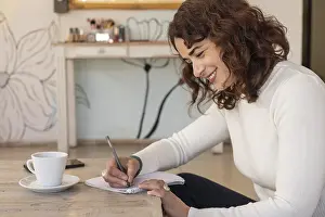 Female Entrepreneurship Drucke: Smiling entrepreneur writes notes in a notebook while working at a table