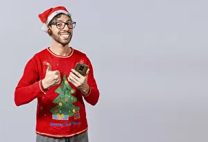 Thumbs Up Gesture Drucke: Smiling guy in christmas hat using cellphone with thumb up
