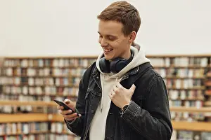 Healthcare System Infrastructure Drucke: Smiling student using smartphone while standing in library