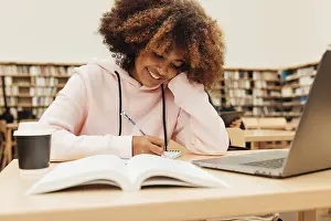 Education And Learning Concept Drucke: Smiling student writing in library