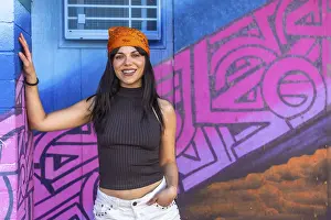 Zeitgenössische Kunst Drucke: Eine lächelnde junge Frau posiert mit Selbstvertrauen vor einem lebhaften blauen und rosa Graffiti-Wall