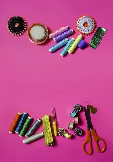 Text Free Space For Copy Drucke: Several spools with cotton threads placed with scissors and set of needles on pink surface