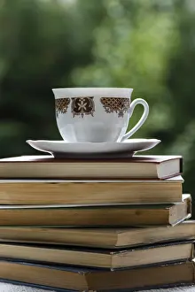 Deserted Garden Table Drucke: Stack of books on table in garden with a tea cup on top