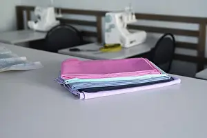 Woman Working Drucke: A stack of colorful fabrics on a table in a sewing workshop