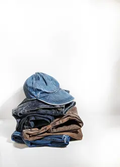 Casual Clothing Drucke: A stack of denim jeans and a baseball cap lie on a white background