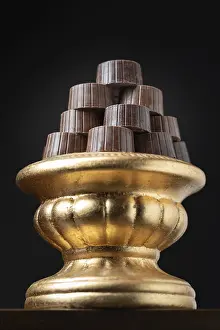 Dark Background Desserts Drucke: Stack of fine chocolates on golden pillar dish with dark background