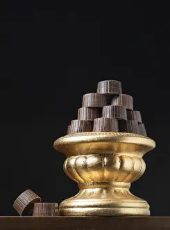 Dark Background Desserts Drucke: Stack of fine chocolates on golden pillar dish with dark background