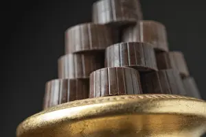 Chocolate Desserts Drucke: Stack of fine chocolates on golden pillar dish with dark background