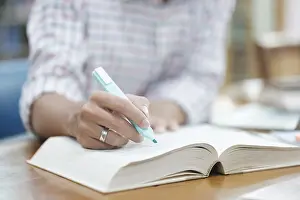 Laptop Computer Use Drucke: A student writes notes in a notebook while studying in a library