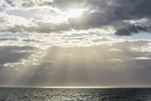 Cloudy Day Europe Drucke: Sun breaks through the clouds with sunrays over sea