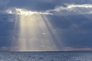 Deserted Coastline Europe Drucke: Sun breaks through the clouds with sunrays over sea